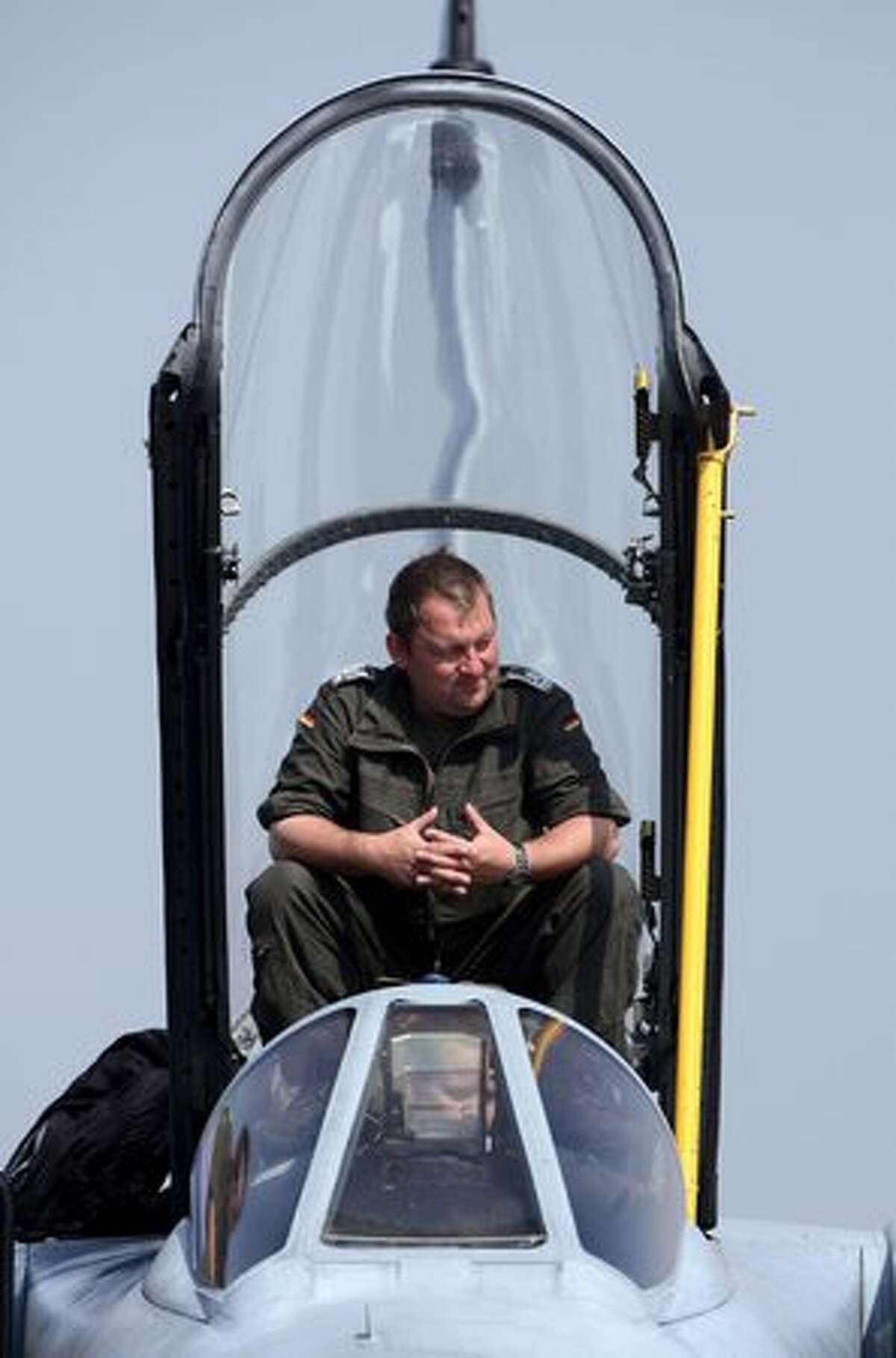 A crew member twiddles his thumbs while sitting over the cockpit and attending to a visitor on a Tornado jet fighter plane at the ILA Berlin Air Show.