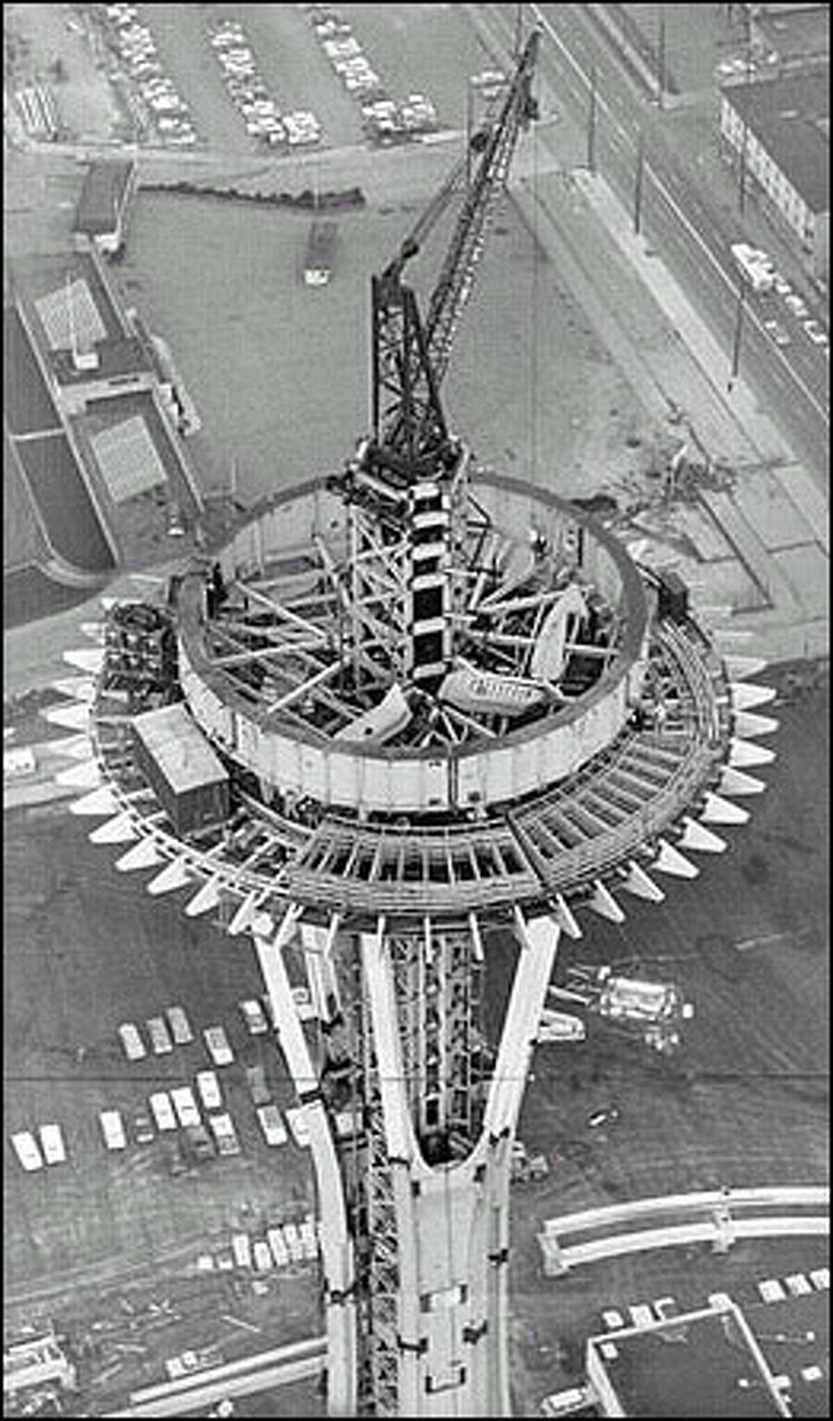 Original caption: "This unusual view of the World's Fair Space Needle was shot by Post-Intelligencer photographer John Vallentyne from a Seattle Police helicopter piloted by Patrolman Gordon D. Grosvenor. Thick ring in center is ring girder to hold out-rigger brackets that will support observation platform. Lattice-like sections in foreground are sections of restaurant turntable which will make one revolution an hour. On ground (bottom of picture, right) are monorail beams on which trains will ride." Photo taken in 1961.
