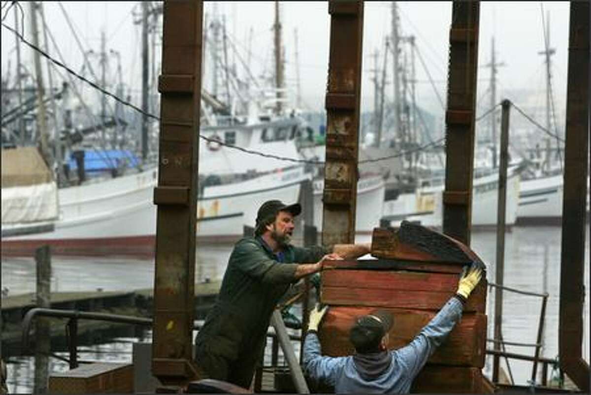 Beach gang crewmen Ernie Mezich (left) and Bill Corey prepare the haul out area to receive a boat at Fishing Vessel Owners Marine Ways, Inc. in Fishermen’s Terminal. The shipyard, which was built in 1919 around the same time as Seattle’s working fleet of halibut boats in the background, is slated for demolition to make way for construction of the monorail’s green line.