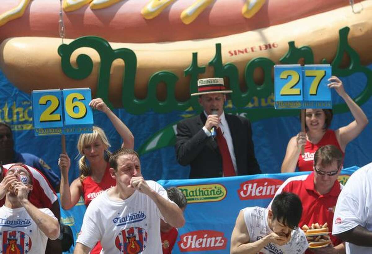 Chairman of Major League Eating George Shea (C-back) speaks as Takeru Kobayashi (R) of Nagano, Japan and Joey Chestnut (2nd-L) of San Jose, Calif., compete. Kobayashi won six previous competitions before tying last year with Chestnut.