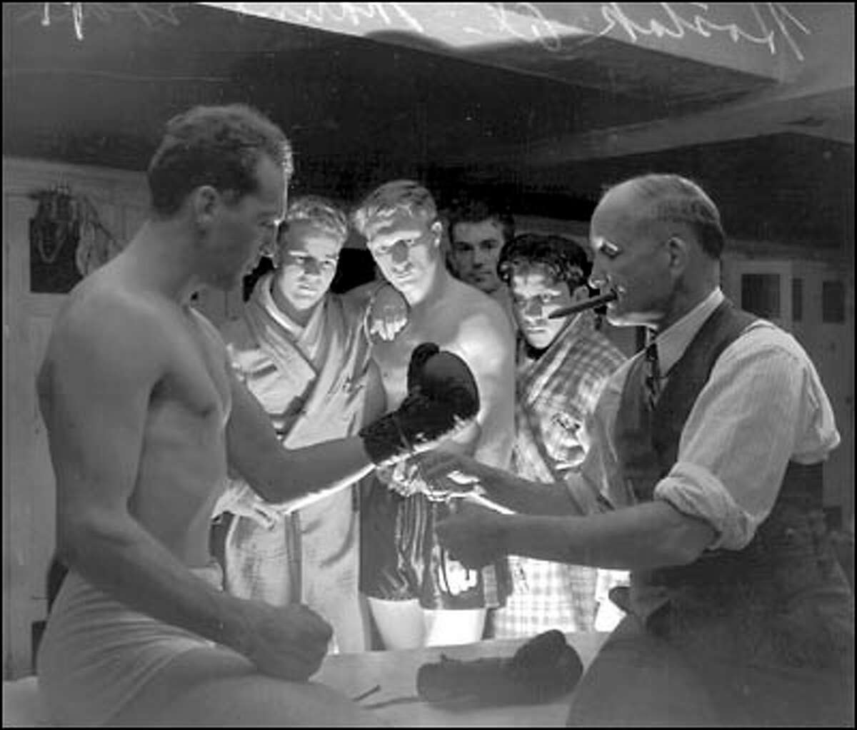 Cigar-chomping trainer Eddie Marino laces up a glove on middleweight titleholder Al Hostak for his Sept. 18, 1938 bout with Young Stuhly at Seattle's Civic Auditorium. Frank "Slim" Lynch lit the scene from below so that a ghostly light plays over the scene.