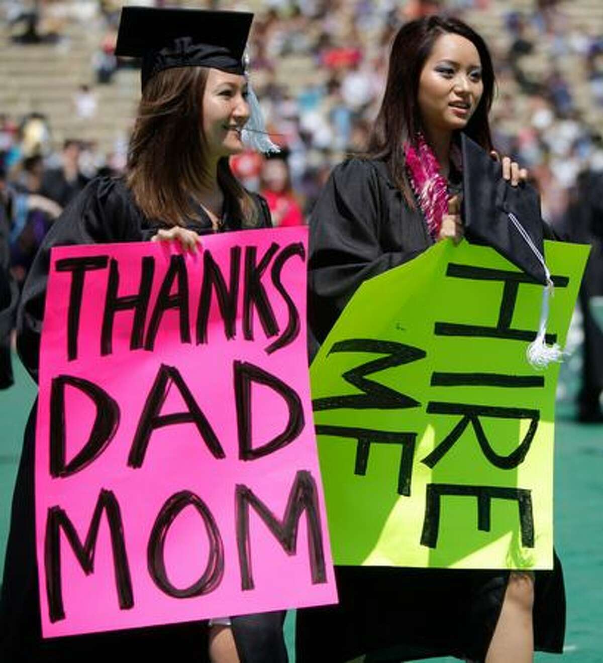 Graduating students Jessica Meurs, left, and Toquyen Truong hold brightly-colored signs while walking to their seats.