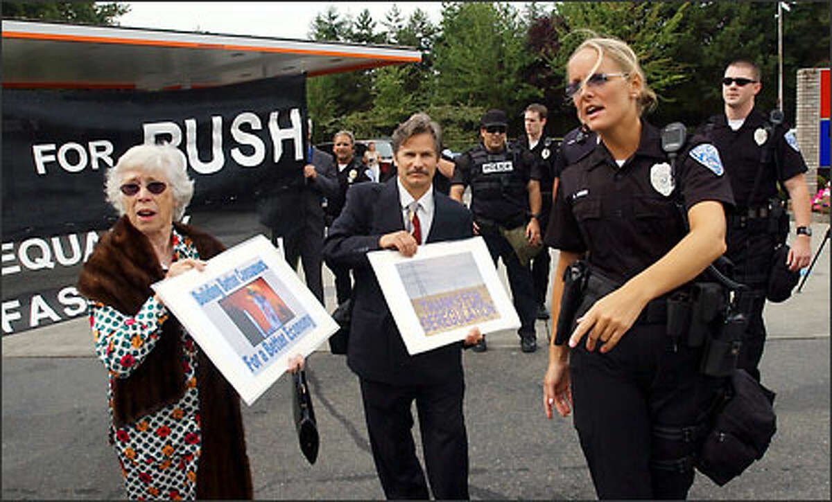 A police officer escorts members of a street theater group calling themselves Billionaires for Bush to a designated protest area in Hunts Point, where President Bush attended a fund-raiser.