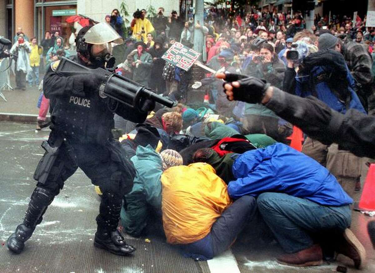A Seattle police officer fires his weapon point blank into a group of demonstrators attempting to prohibit access to the WTO at the intersection of Sixth Avenue and Union Street on Nov. 30, 1999, outside the Seattle Sheraton. Police first informed the demonstrators that they were in violation of an order to disperse.