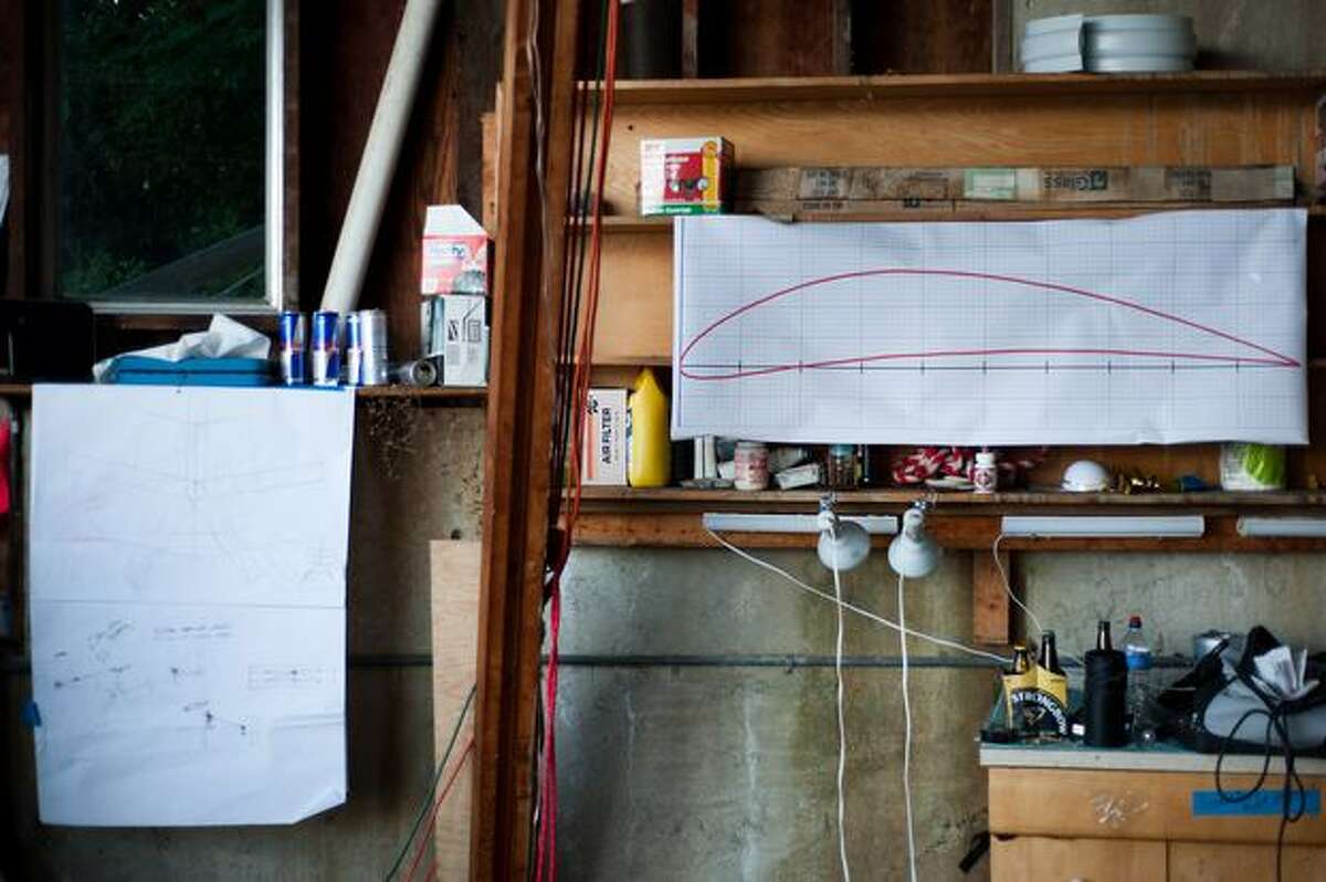 Plans and diagrams showing the design of the aircraft are scattered throughout the garage.