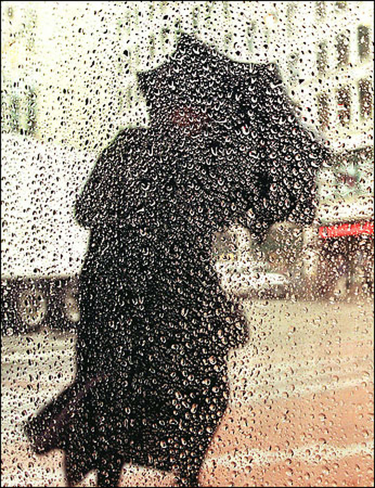 A pedestrian uses an umbrella as a shield against the wind and the rain on the corner of Pike Street and Fourth Avenue in downtown Seattle.