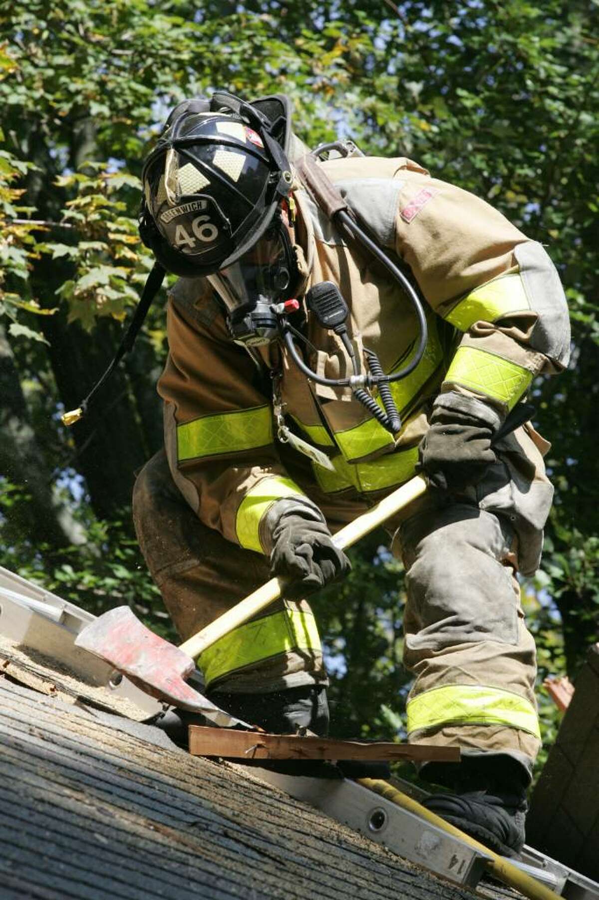 Greenwich firefighter Tony Schell uses his axe to chop through a roof during a training excercise Friday morning.