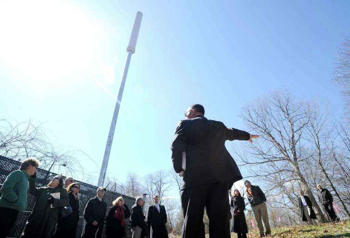Foreground, Carlo Centore of Centek Engineering of Branford, Conn., explains plans for a new cell tower that would replace the exisiting 70-foot AT&T "flag pole"-style cell tower, pictured. The Connecticut Siting Council and interested parties listen during a tour of the site of the proposed Verizon Wireless 77-foot cell tower, at 36 Ritch Ave., Byram, Tuesday afternoon, March 29, 2011. The new tower would be designed to look like a pine tree.