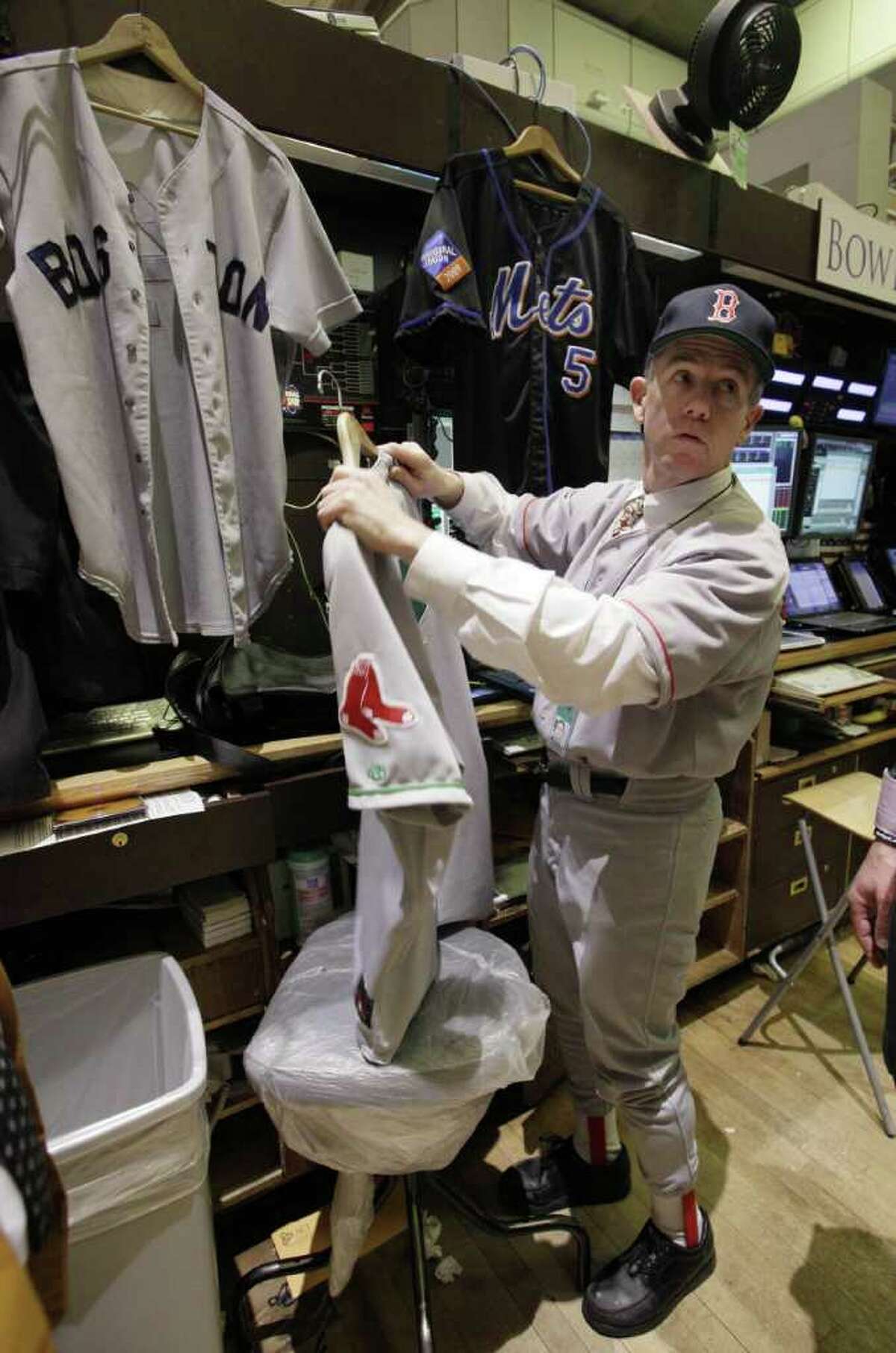 Michael Quinn, with Bowers Securities, is dressed in Boston Red Sox uniform, and sorts through other of his baseball jerseys, as he works on the floor of the New York Stock Exchange, on Major League Baseball's opening day, Thursday, March 31, 2011.