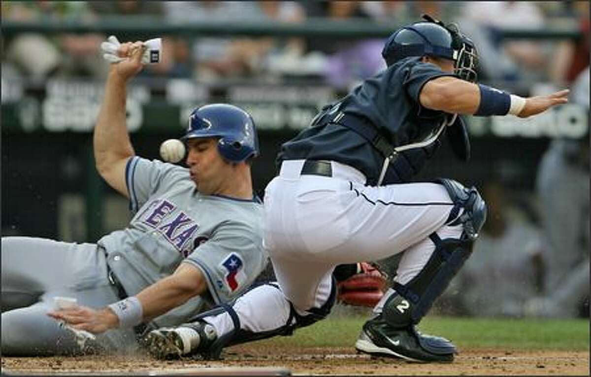 Seattle Mariners Kenji Jojima misses the ball as Texas Rangers Mark Teixeira slides into home to score on a Marlon Byrd single during third inning action at Safeco Field.