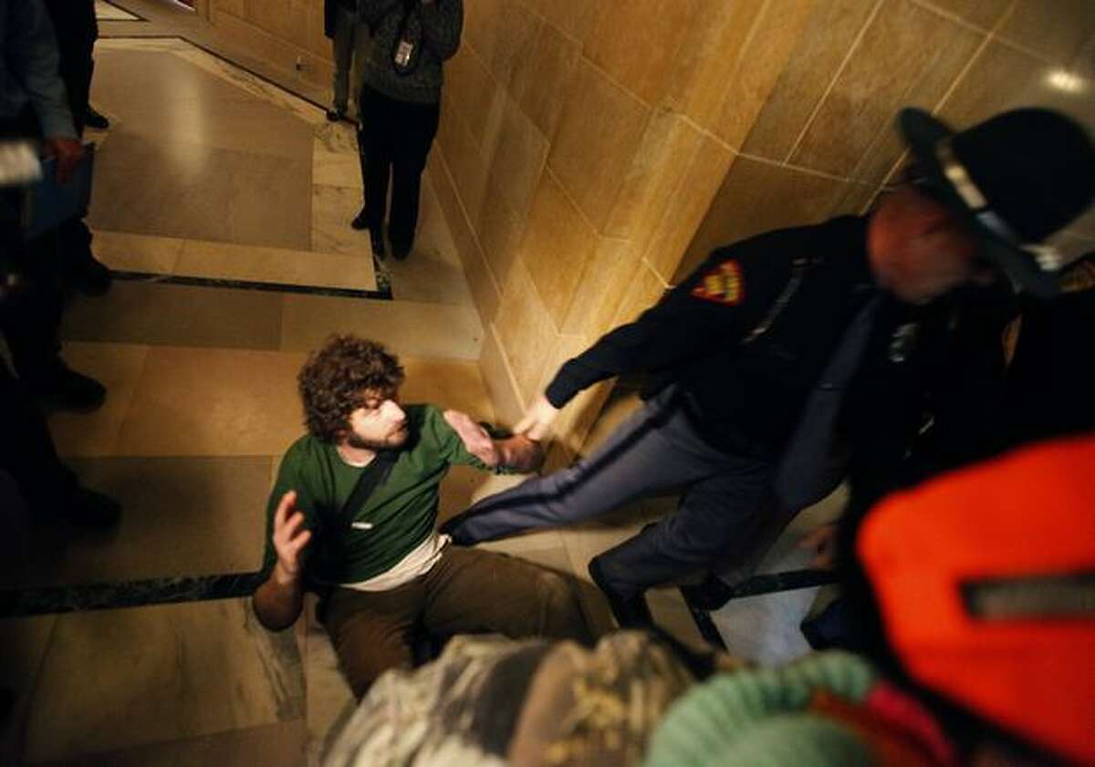 Owen Curtis is escorted out of the Wisconsin State Capitol Assembly Room lobby by law enforcement personnel on Thursday after spending the night in the room with demonstrators opposed to Gov. Scott Walker's budget repair bill, in Madison, Wis. Tensions have flared after Republican senators passed an amended version of the controversial bill which largely strips collective bargaining for public employees. (AP Photo/Wisconsin State Journal, John Hart)