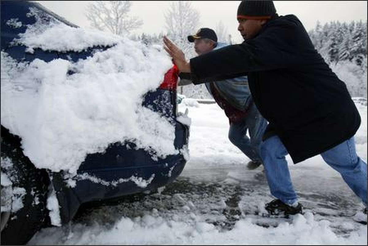 Brian Salmon, left, from Lynnwood, and Jose Romero, from Issaquah, help Jeff Pickel (not shown) drive his car out of the snow from the East Sunset Way exit off Interstate 90 in Issaquah. Pickel was one of many motorists who abandoned their cars during Wednesday night's snowstorm.
