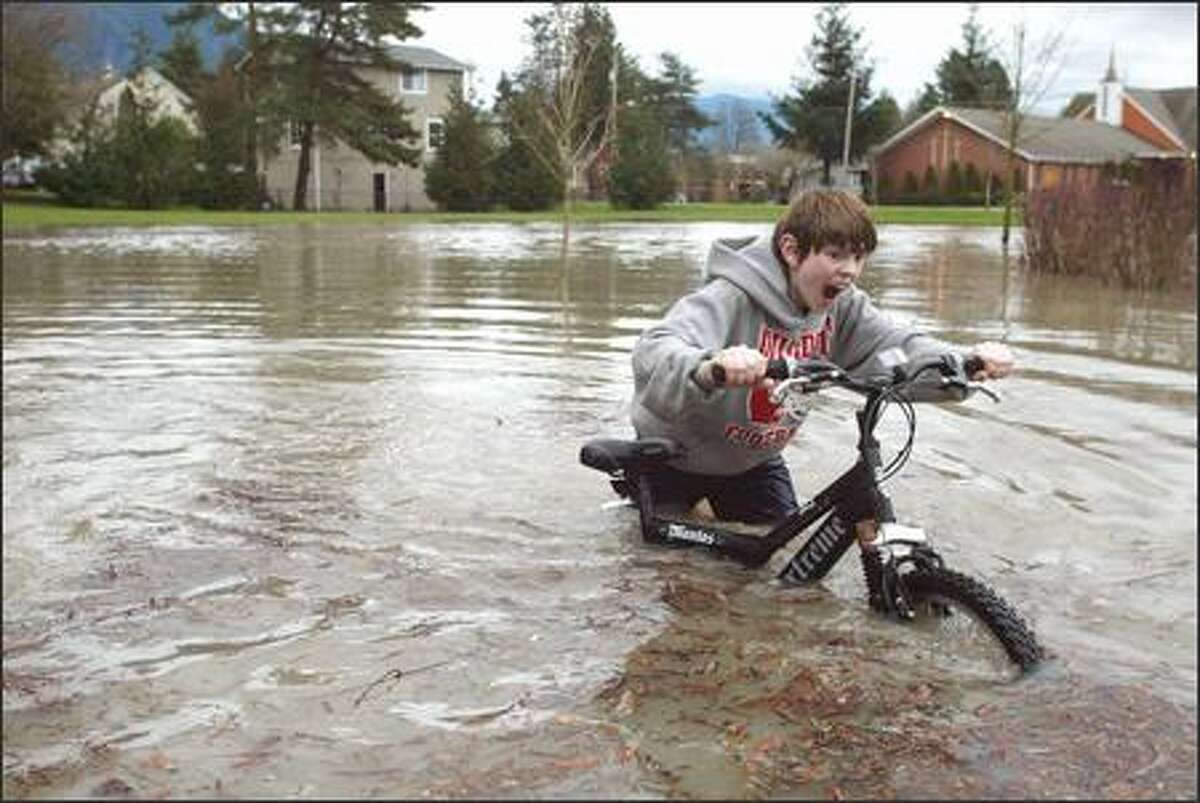 Chris Conley, 12, pushes his bike through a flooded portion of River View Park next to the Snoqualmie River in Snoqualmie. The rain brought with it a record high of 60 degrees at Sea-Tac Airport.