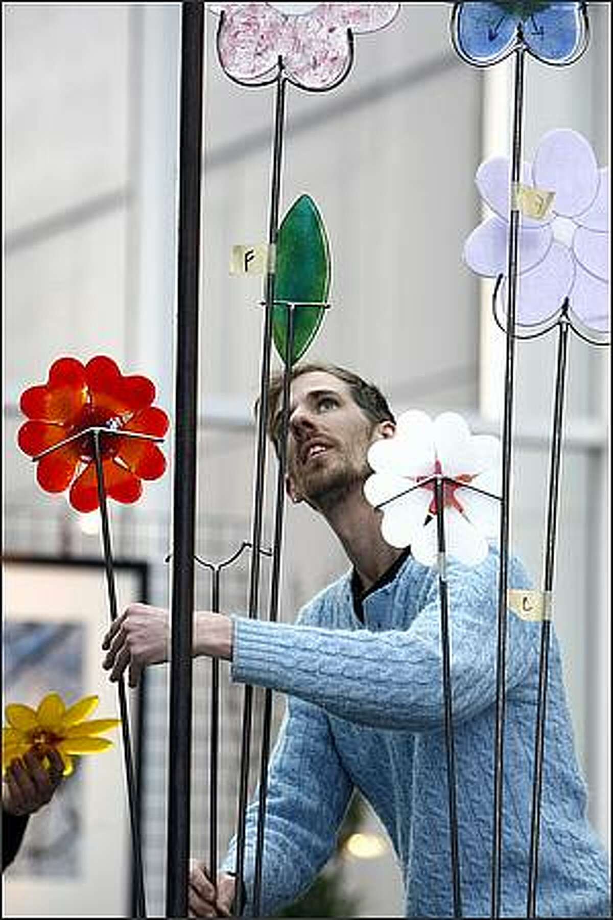 Greg Baker, of Bedrock Industries, sets up their "Bee Here Now" display in the skybridge of the Washington State Convention and Trade Center for The Northwest Flower & Garden Show. The garden stake flowers are made of 100 percent recycled glass.
