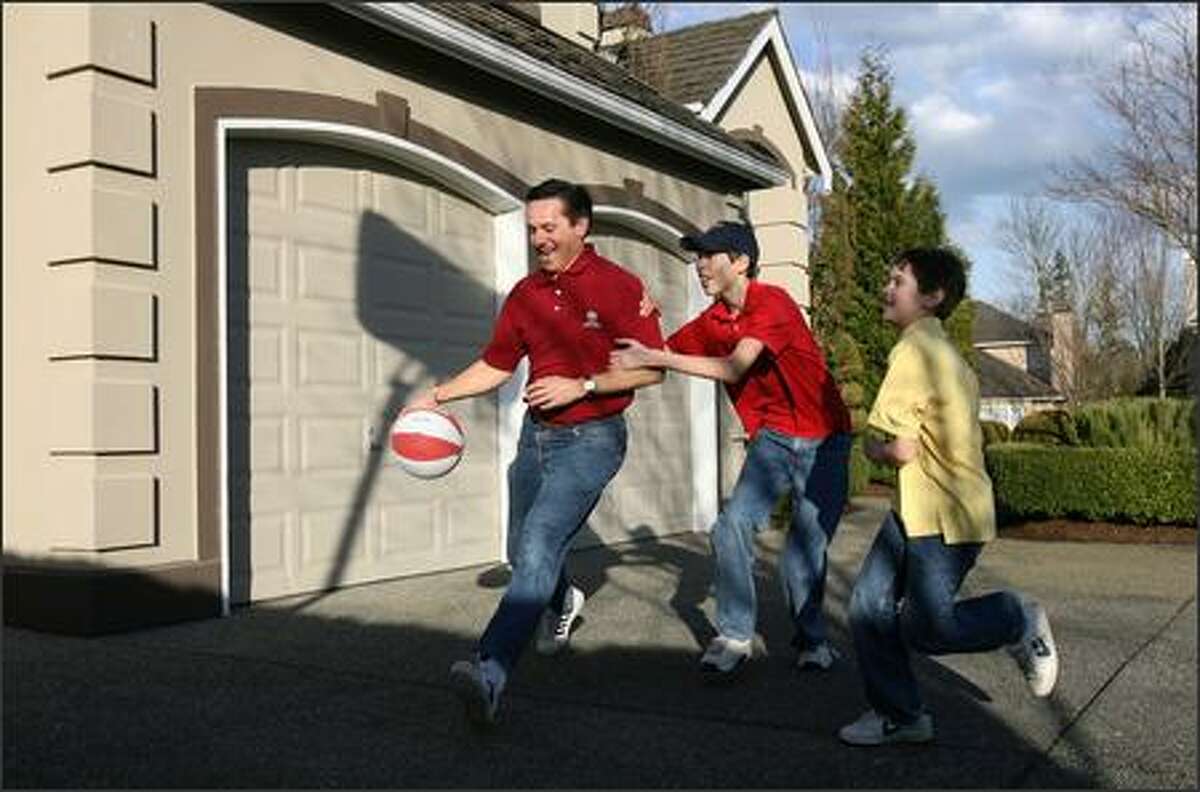Dino Rossi is fouled by his son, Jake, 13, while his other son, Joseph, 10, runs to get in on the action as they shoot hoops in the driveway of their Sammamish home.