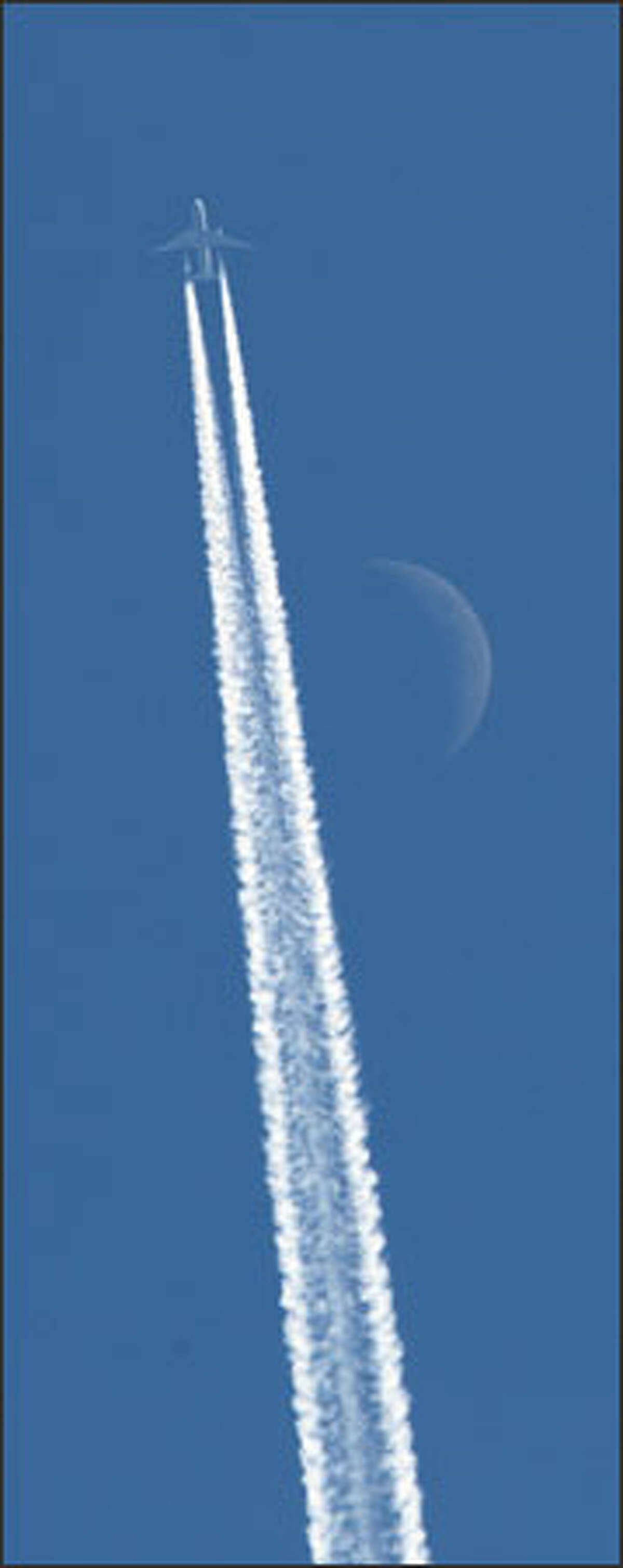 With a faint moon above, a jet leaves its contrail across another brilliant blue sky over Western Washington.