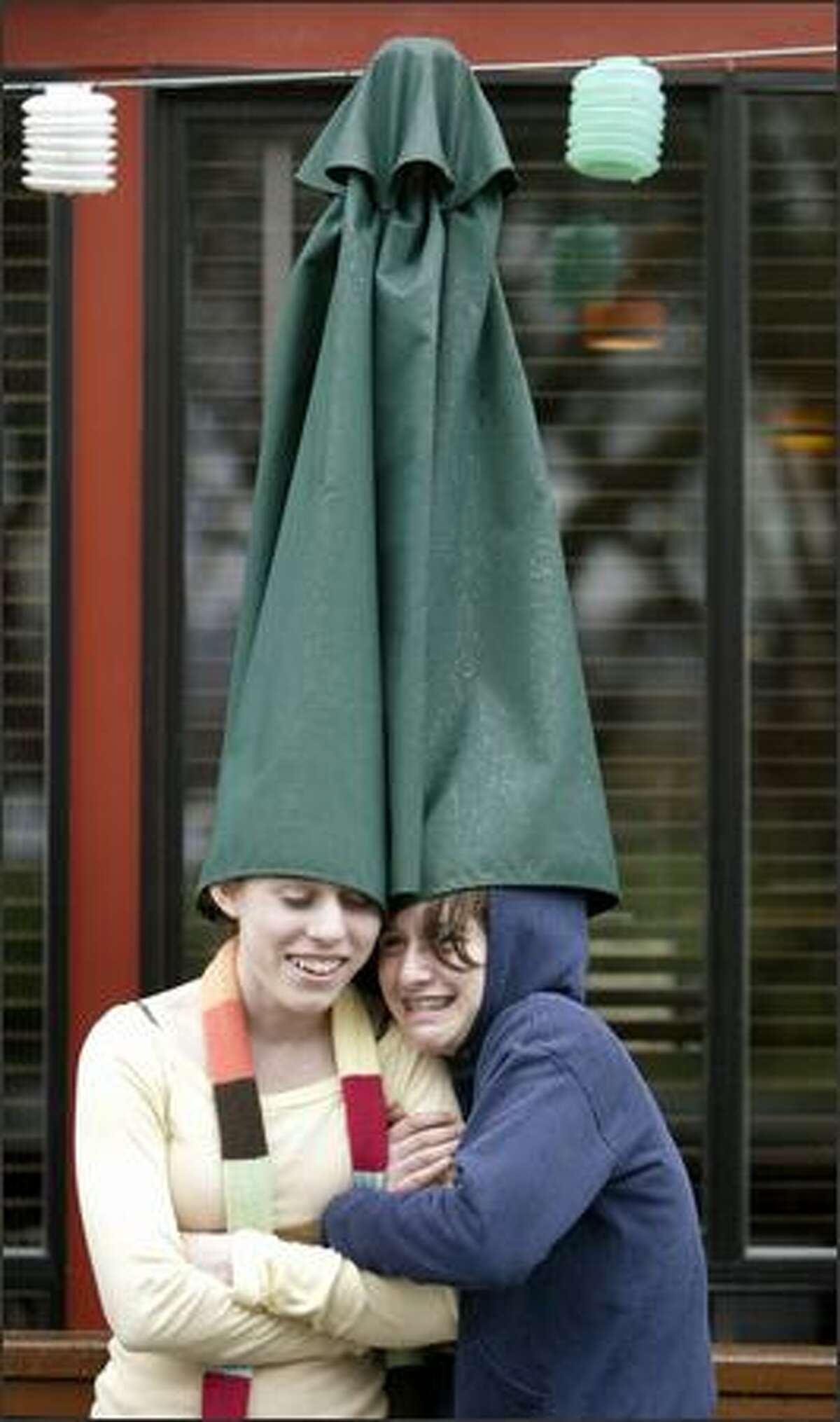 Alea Christiansen, left, and Kate Baron, both eighth-graders at Billings Middle School, get a little creative as they use a patio umbrella to try to keep dry while waiting to enter the Green Lake Bar & Grill in Seattle on Wednesday. The school, in a partnership with the restaurant, exchanges weekly hot meals for students for parking space for the restaurant’s patrons. Today, that rain will be back.