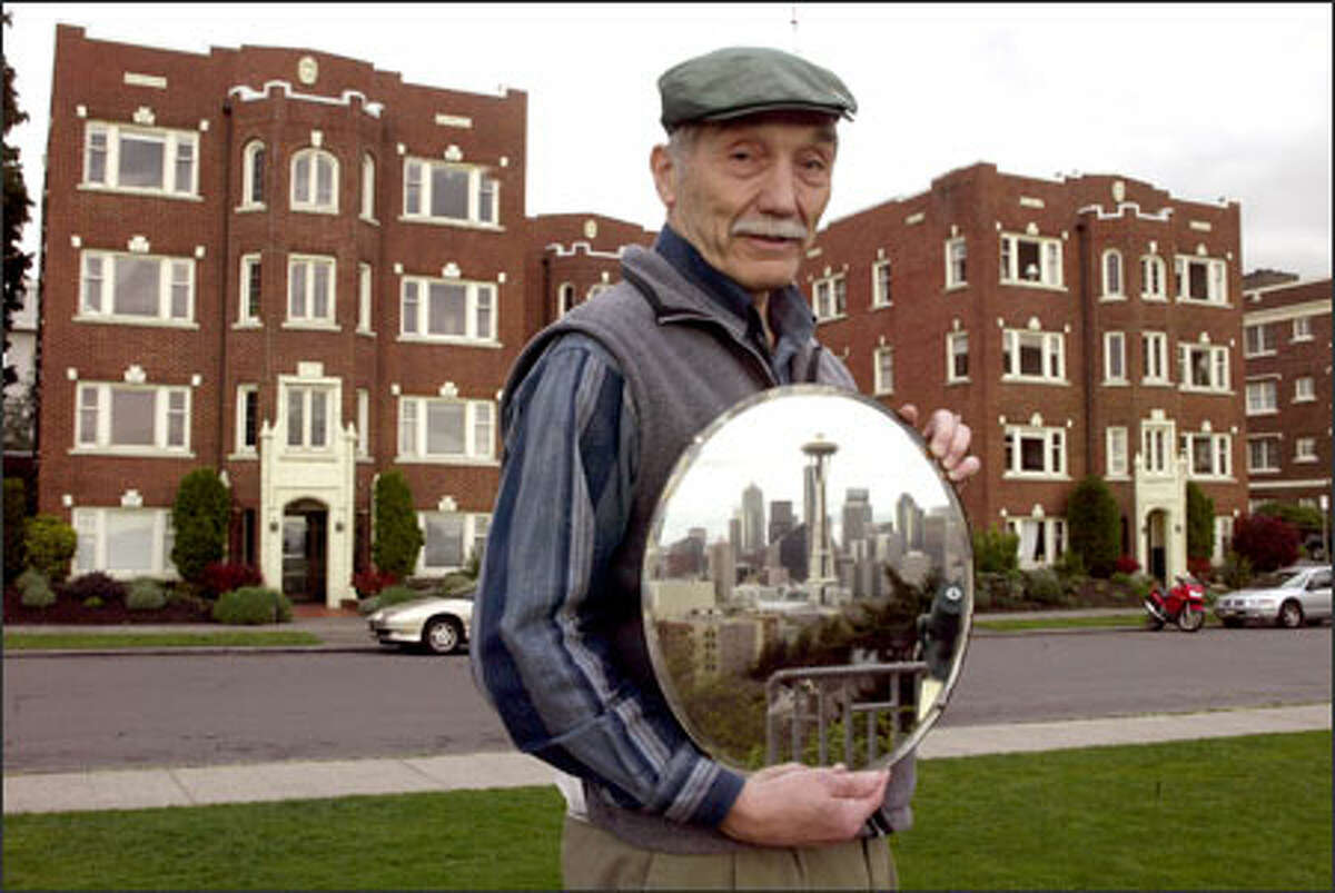 John Hennes, in Queen Anne's Kerry Park, holds a mirror reflecting the Space Needle as he stands in front of 1920s apartments slated to be torn down. Neighborhood residents are lobbying the city of Seattle to impose guidelines on new development.
