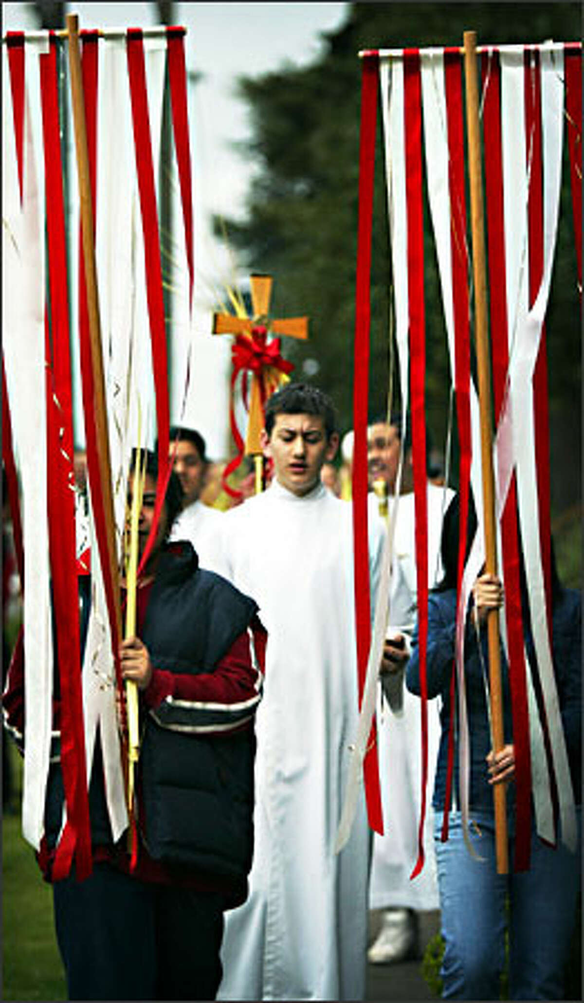 A parishoner holds a cross made from a palm frond during a Palm Sunday procession at St. George Parish in south Seattle on Sunday. Parishoners walked from St. George’s School to the church down the block, carrying palm fronds and singing in celebration of Palm Sunday. Palm Sunday is celebrated as the day that Jesus entered Jerusalem and begins a holy week that ends with Easter Sunday.