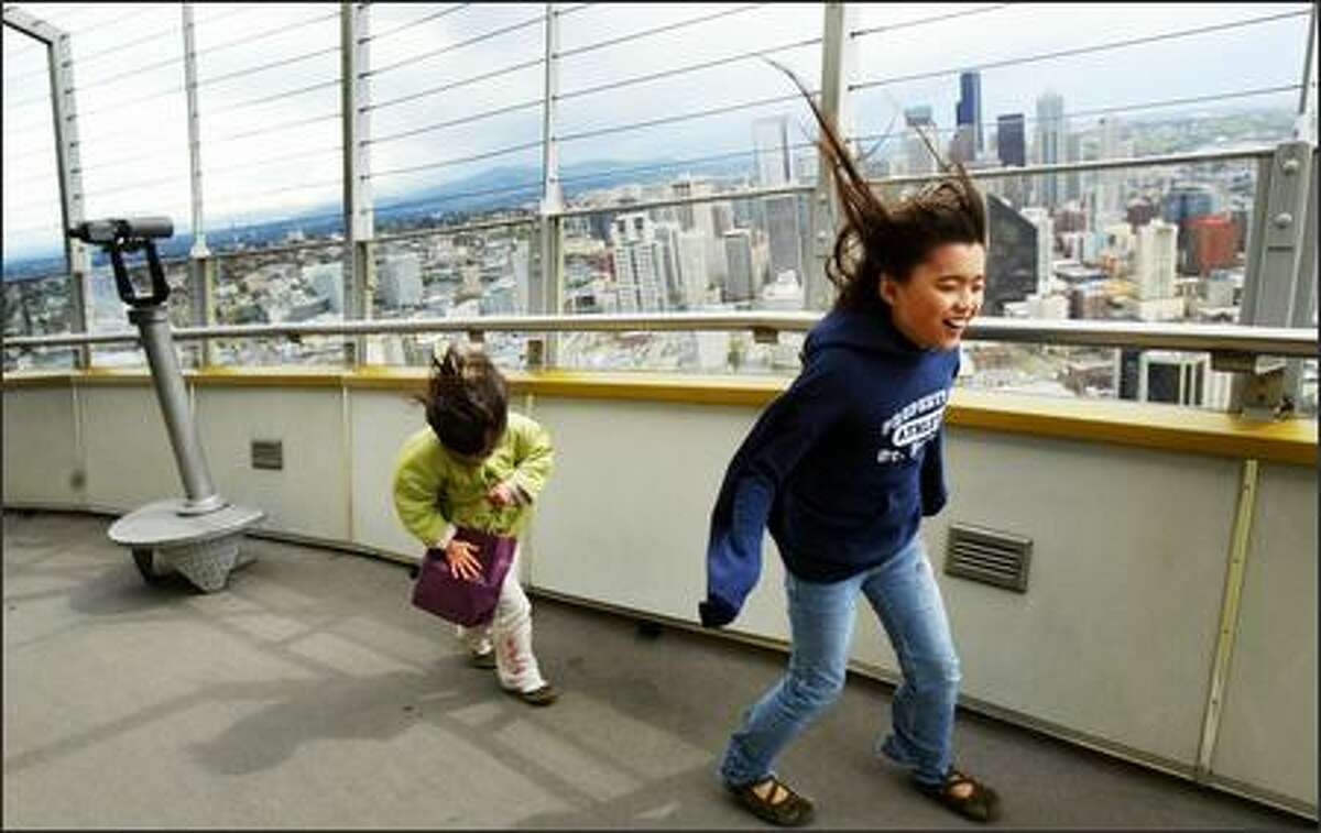 Alyssa Fruge-Culanag, 9, and her younger sister Remy, 5, try to stay upright while pushing through a stiff wind while walking laps around the top of Seattle's Space Needle on Monday. High winds blew around the region during the morning and into the afternoon.