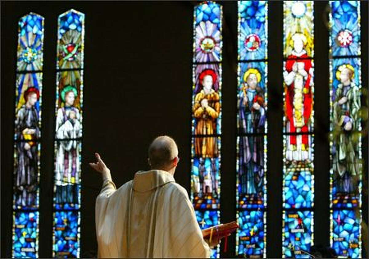 The Rev. Christopher Weekly, S.J., preaches to his parishioners under the watchful gaze of the apostles depicted on stained glass windows at St. Joseph Catholic Church.
