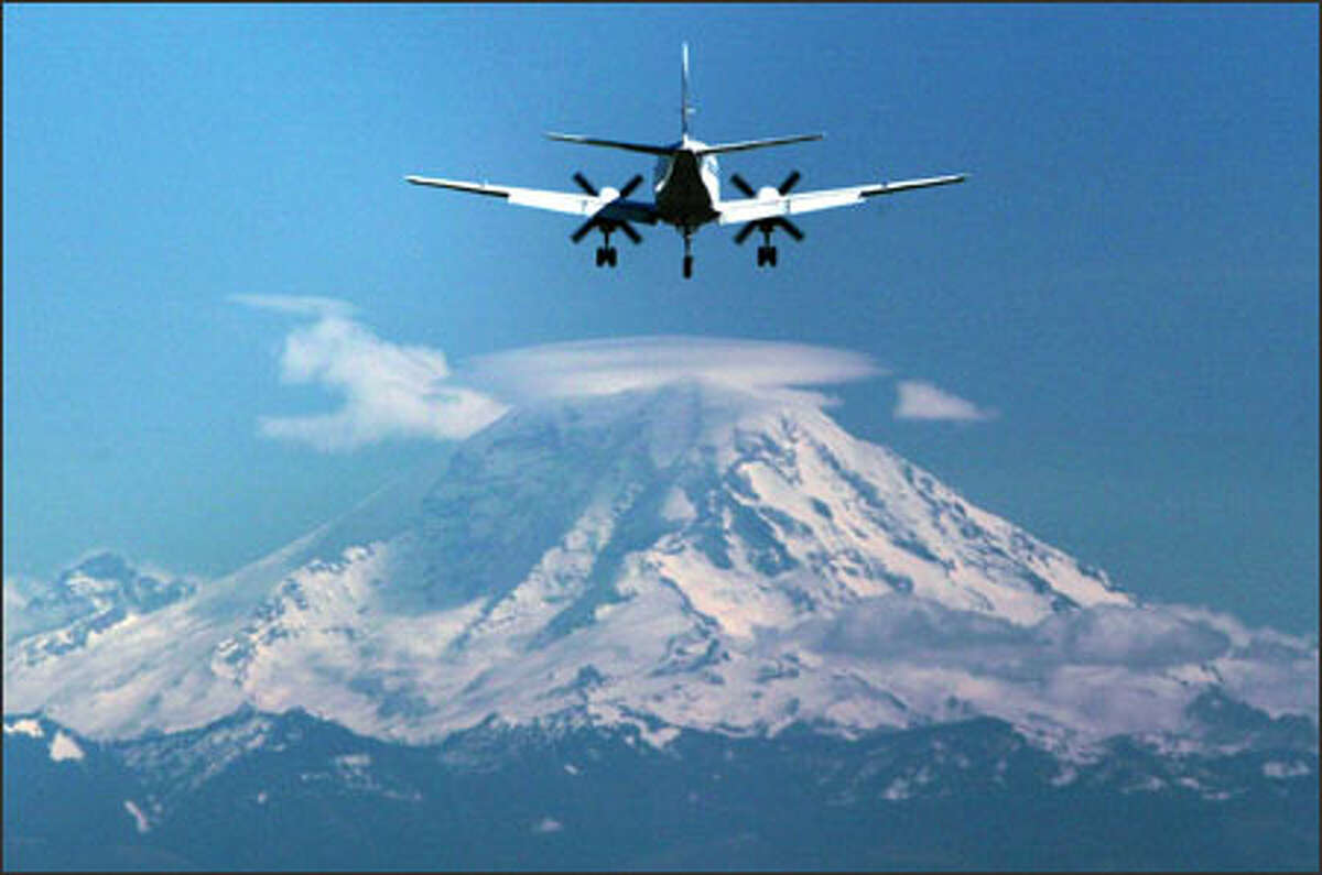 A civilian turbo prop plane heads for a landing Thursday at Boeing Field as a lenticular cloud clings to the top of Mount Rainier.