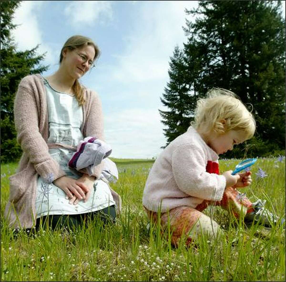 Two-year-old Thea Byrne looks at a camas through a magnifying glass at the Glacial Heritage Preserve near Littlerock as mom Gabby looks on.