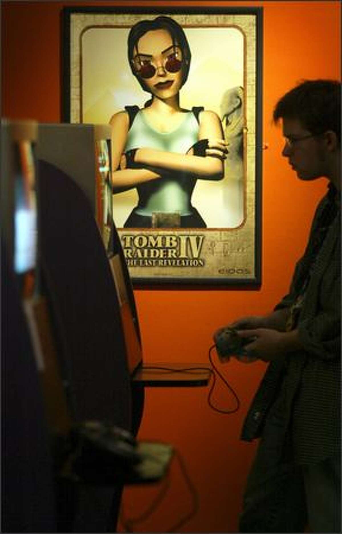 Lara Croft of the "Tomb Raider" video-game series keeps an eye on Pacific Science Center staffer Geoff Nunn as he plays one of the games during a preview Thursday of the exhibit "Game On: The History, Culture and Future of Video Games." The exhibit runs through the end of August.