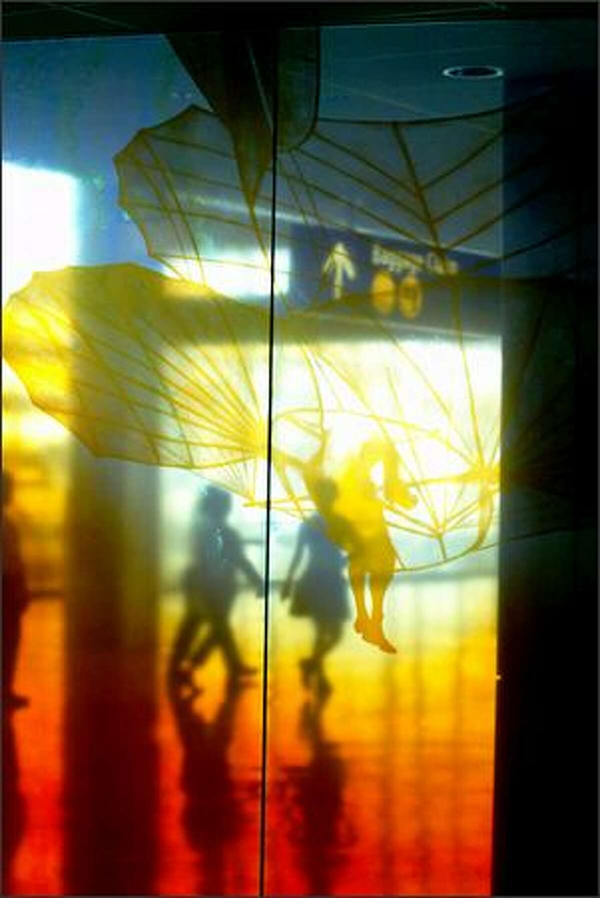 Passengers pass by the new amber glass wall installation that also serves as a security wall in the new Sea-Tac Concourse A. Linda Beaumont's "Traveling Light" comprises 82 painted and silk-screened glass panels.