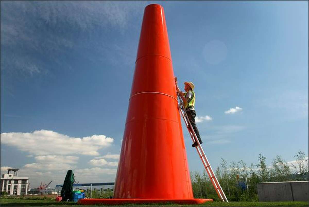 Richard Shanks takes advantage of Thursday's blue skies and applies polish to Dennis Oppenheim's "Safety Cones," a temporary exhibit at the Olympic Sculpture Park. "Safety Cones" will be on display through October. The artist is described as someone who "playfully manipulates scale and everyday objects."