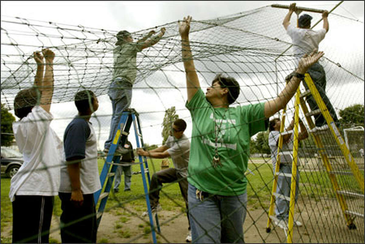 Carmen Martinez, center right, the teen development leader with Seattle Parks and Recreation, helps parent and neighborhood volunteers erect a batting cage yesterday at the South Park Community Center.