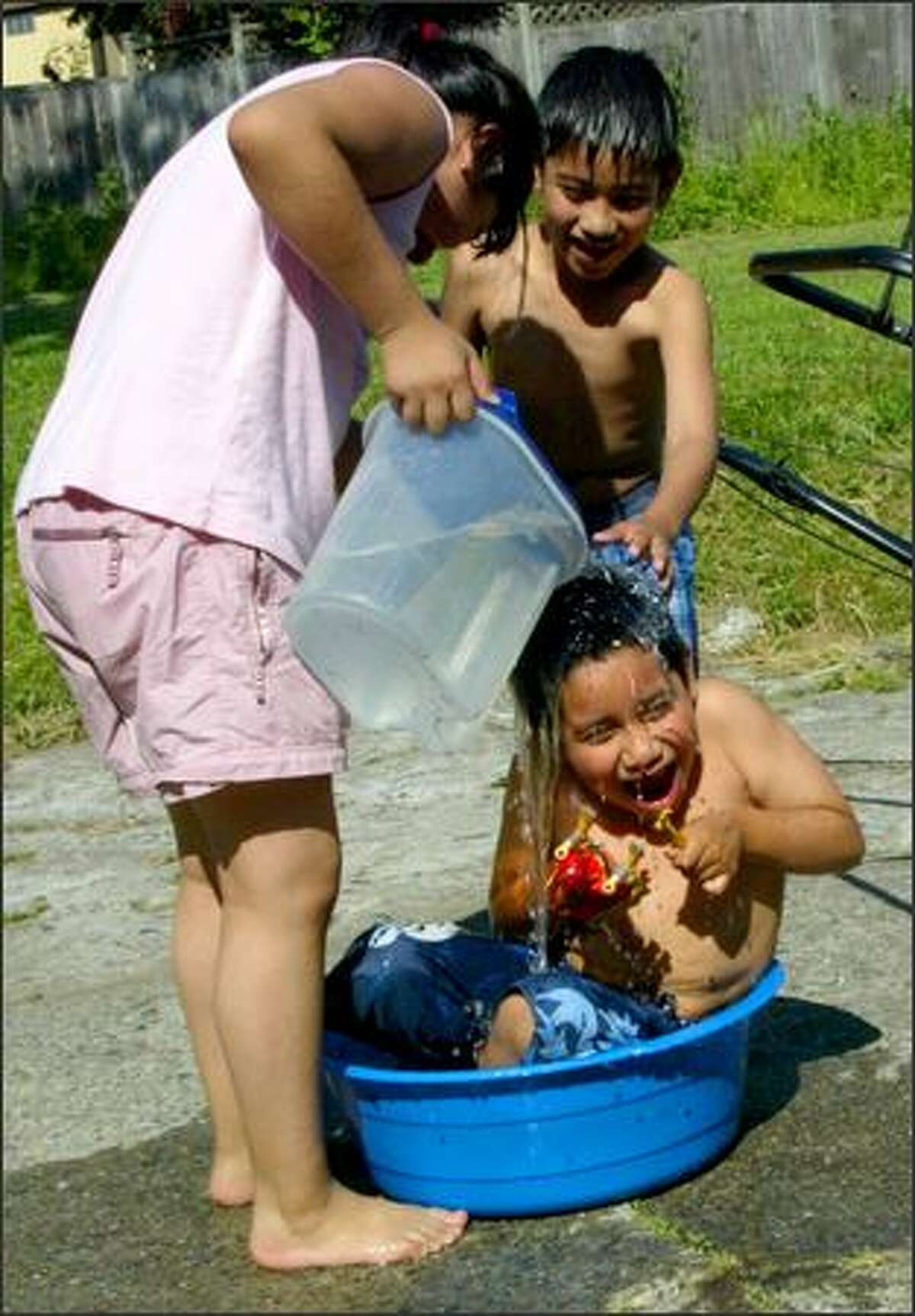 Eleven-year-old Miriam Mendoza and her brother, Irving, 9, "help" their younger brother, Axel, 6, keep cool in Monday's heat. The children were playing outside their mom's work.