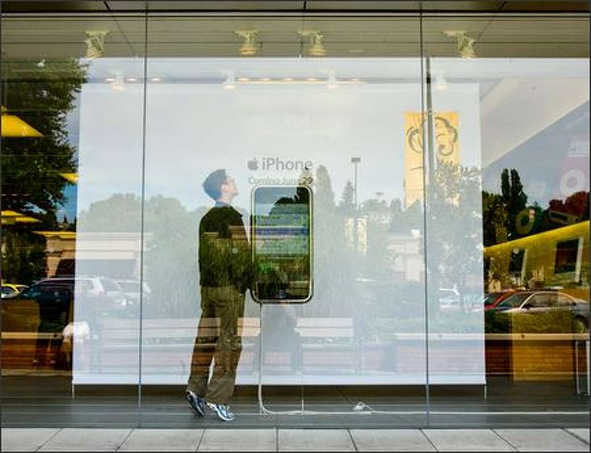 David Kim, on break from his job at Childrens Hospital, steps inside the display window at the University Village Apple Store to check out a large image of the new iPhone. Kim says he's interested in getting one but has to wait until his service contract on his present phone runs out this fall. The widely anticipated iPhone was officially released for sale at 6 p.m. Friday.
