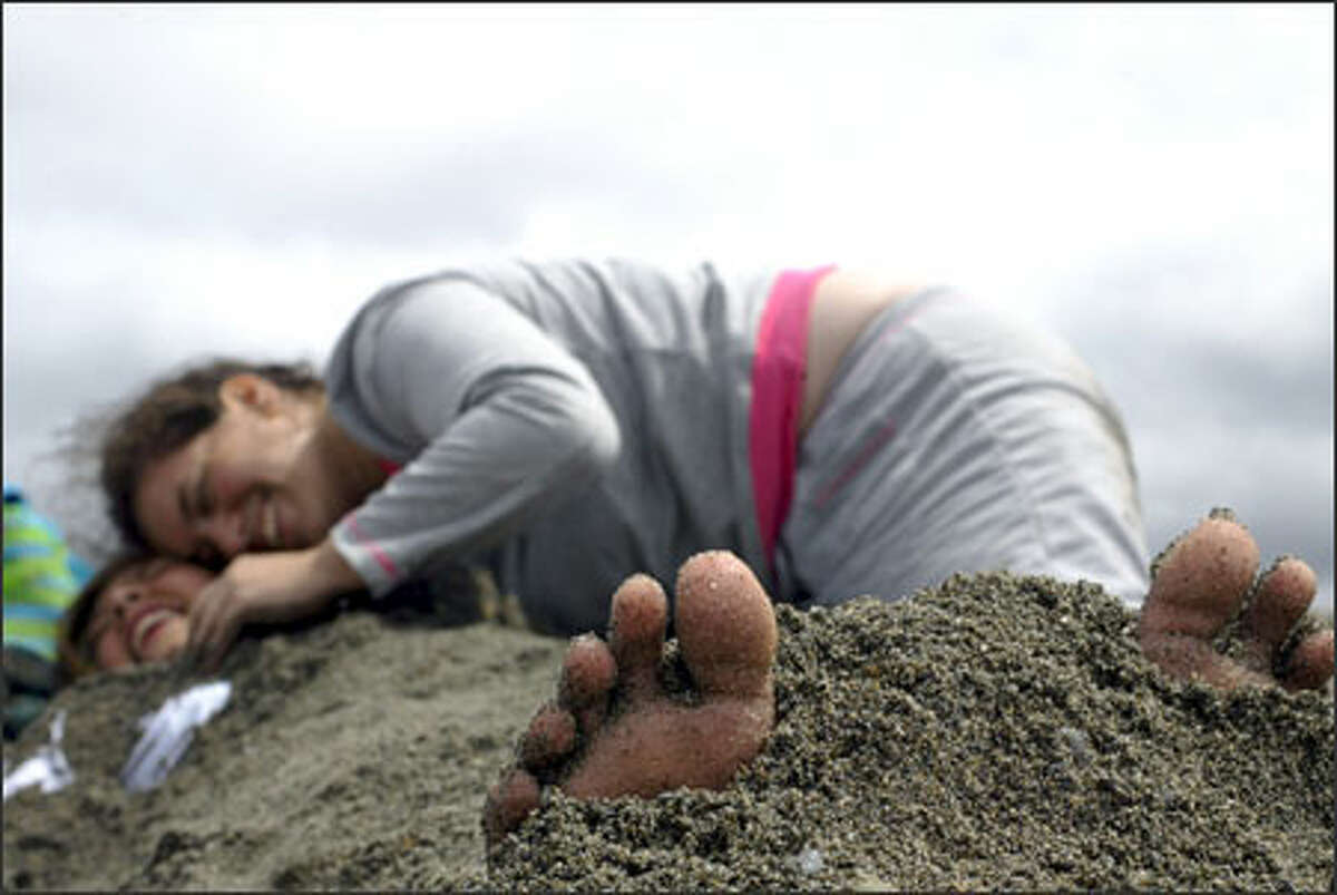 Amber Rosenberg, 17, right, buries her friend, Ashlie Adams, 17, both of Lynnwood, in the sand Wednesday during a sand-sculpting contest at Marina Beach in Edmonds. The annual sand-sculpting contest sponsored by Edmonds Parks and Recreation attracted about 100 children and parents despite a short downpour and a lot of wind.