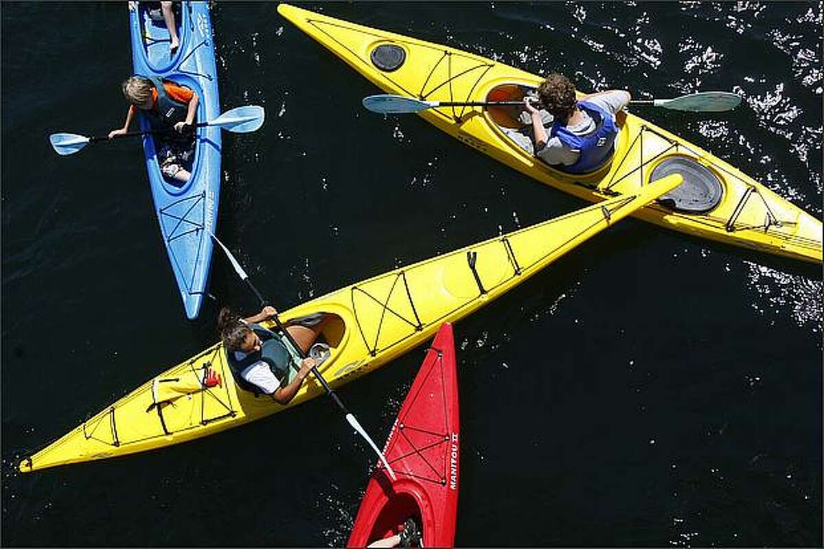 A group of kids and instructors from the Moss Bay Kids Camp converge beneath the South Lake Union Park footbridge while playing a game in their kayaks.