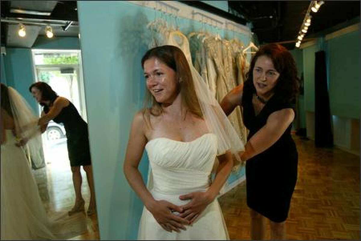 Erica Stillner tries on wedding dresses at the Belltown Bride, a couture bridal outlet owned by Melissa Albert (right) which sells wedding dresses for at least 50% off but come in limited sizes.