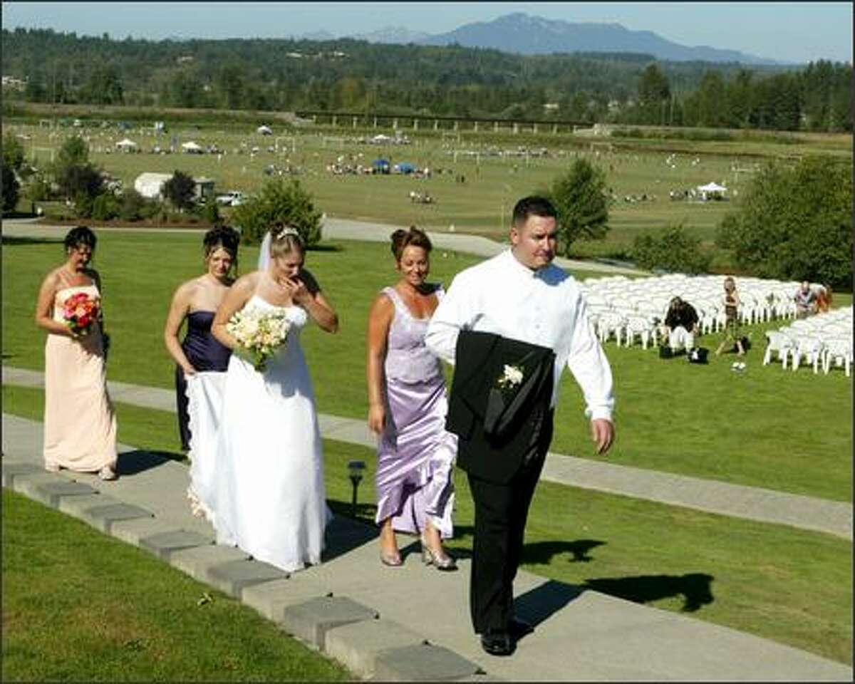 Groom Jim Lambro, followed by his mother, Julie Hunter; bride-to-be, Rachelle Stinde; Katrina Stinde, holding the bridal train; and the bride's mother, Bev Stinde, return from taking wedding pictures at Lord Hill Farms. A soccer tournament is in the background.