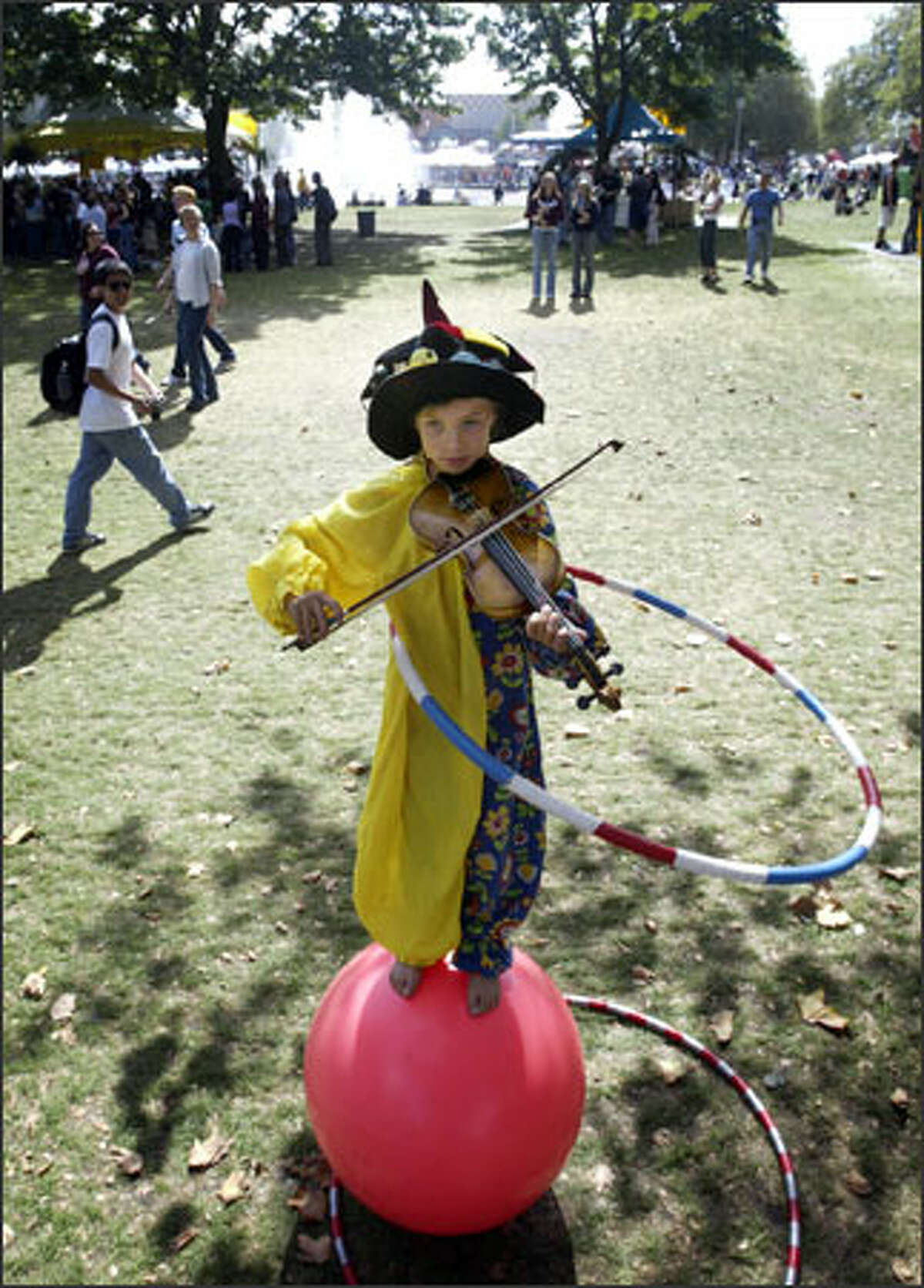 Balancing on a rubber ball and twirling a hula hoop, 9-year-old Una Bennett plays the violin at Bumbershoot. She and her juggling brother, Ezra Weill, 12, can earn $200 to $300 a day.