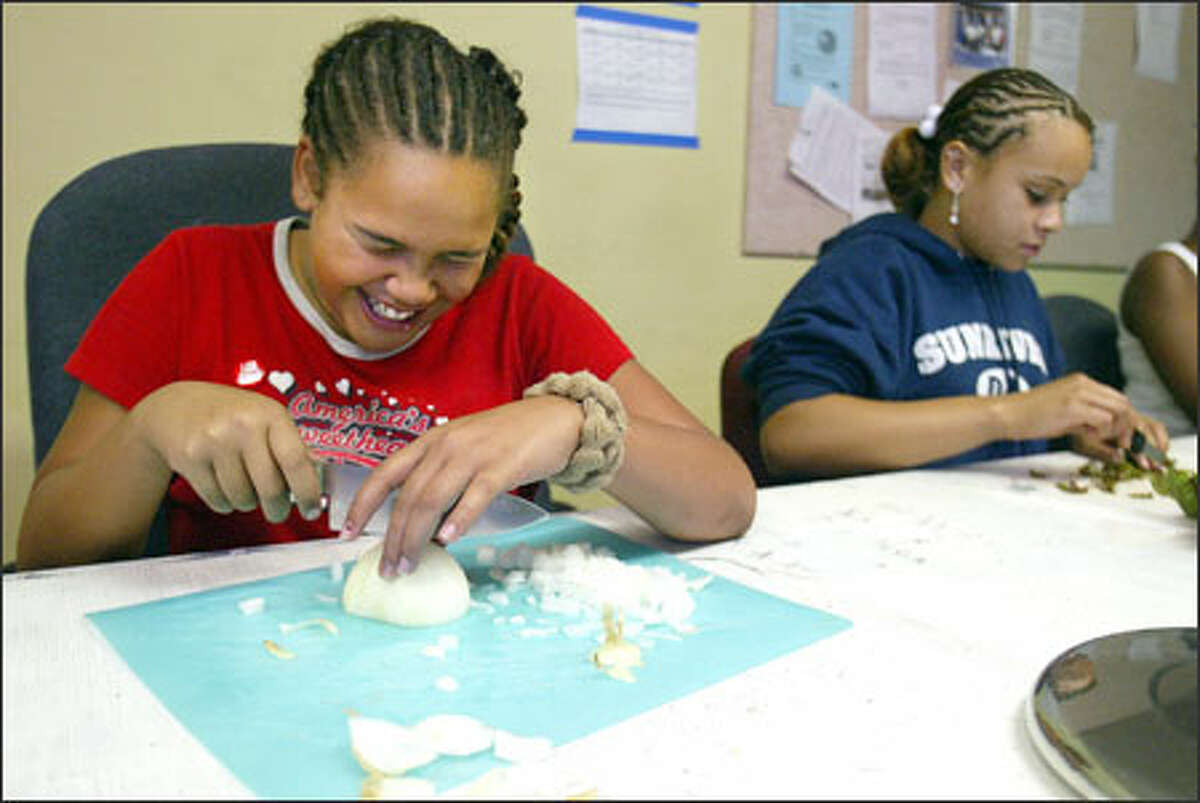 Mariah Williams, left, laughs -- and cries -- as she chops onions and Amari Ray cuts chard as they fix healthy meals in a King County S.N.A.C. class.