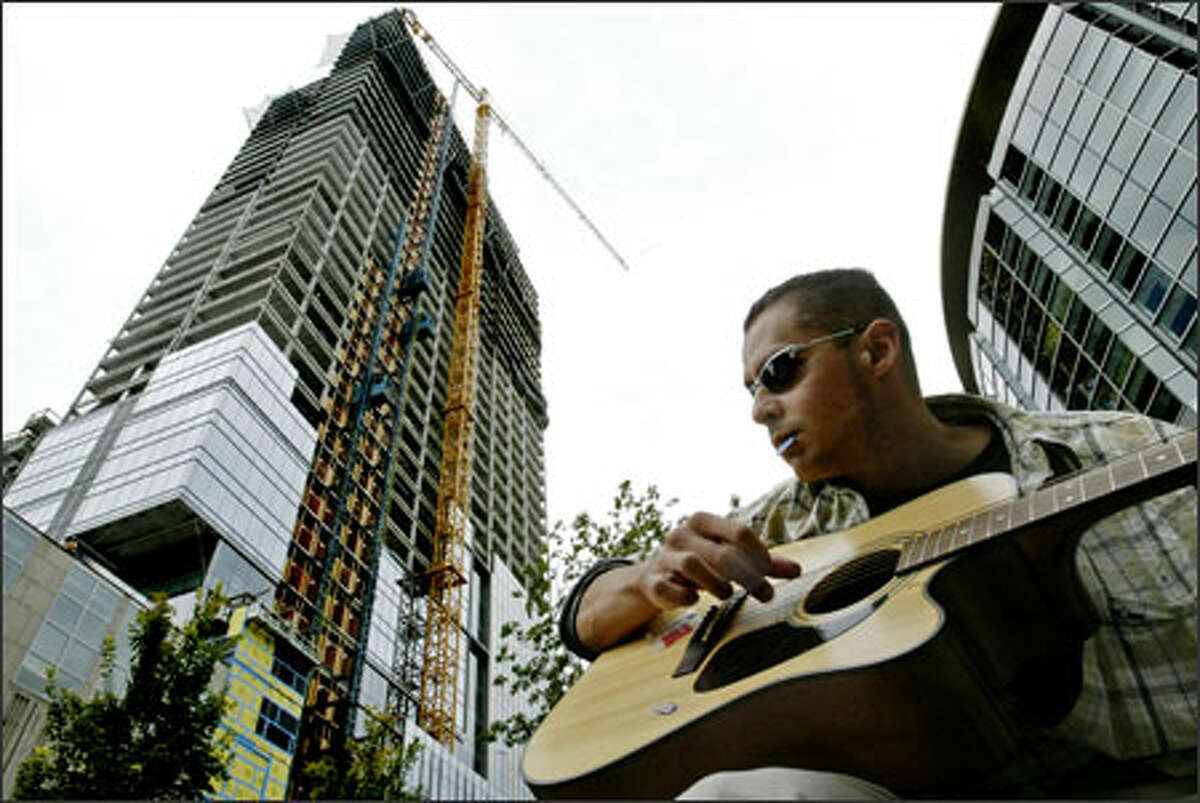 Chris Pittman of Chico, Calif., strums outside Benaroya Hall, with the future Wamu Center above him. The center will increase downtown office space significantly.