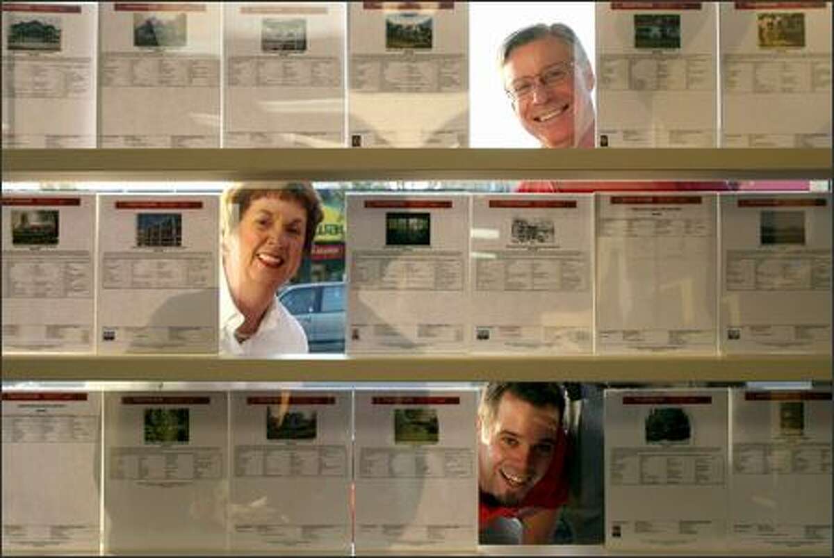 From top, Keller-Williams Realty agents John Thompson, owner/associate broker, his wife Barbara Thompson, lead buyer specialist, and their son David Thompson, lead buyer specialist, look through a few listings in the front window of their West Seattle office.