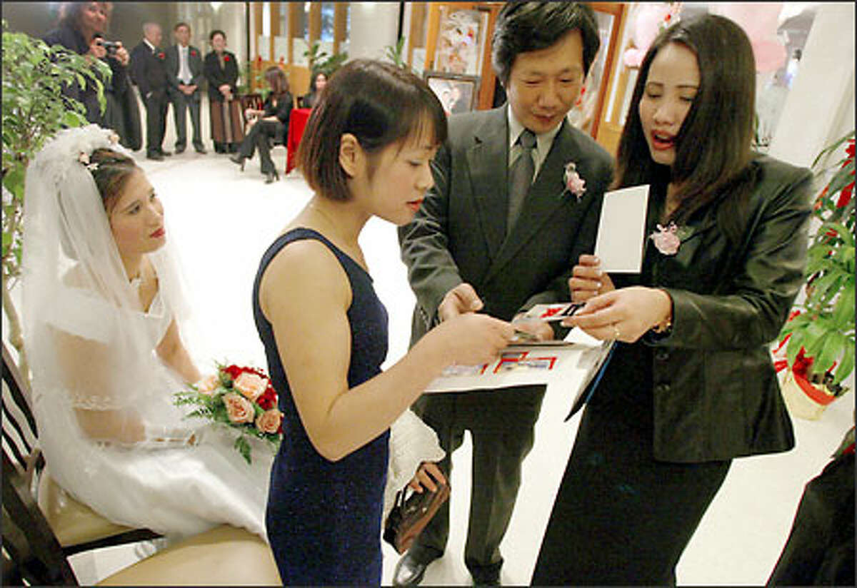 Nga Cao, far left, watches friends she made on American Samoa, Nhung Nong and Giang Hoang, far right, look at photos with Hai-Tri Le, center, as they wait for her wedding banquet to begin.