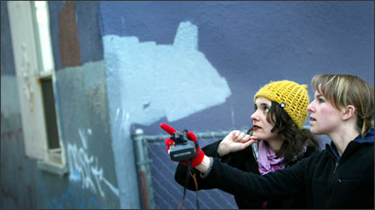 University of Washington doctoral candidate Giorgia Aiello, left, and undergraduate student Emily Fischer contemplate graffiti in an alley behind University Way Northeast businesses as a buffed, or repainted, wall rises behind them. The graffiti are documented before being painted over.