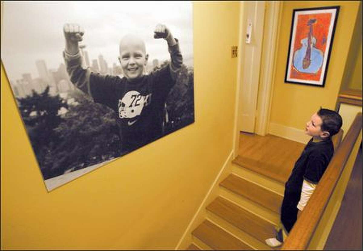 Max Hanson, who is recovering from brain cancer, gazes at a photograph taken by his mother after his final chemotherapy treatment. The photo shows him holding his arms up like a triumphant prizefighter, dwarfing the Seattle skyline behind him.
