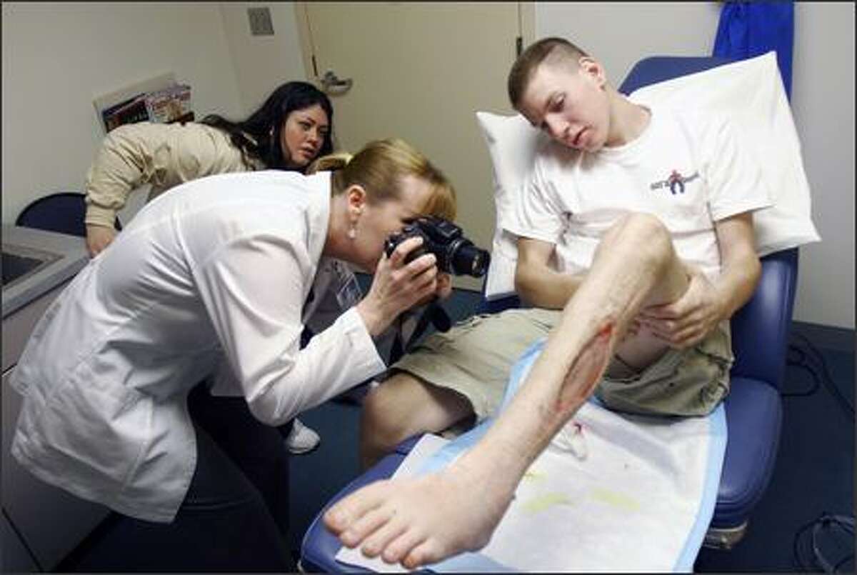 Wendy Vick, clinic nursing supervisor at Providence Everett Medical Center, takes pictures of Brett Karch's wounds. Karch, a member of the Snohomish High School ROTC team that was manning a cannon at a football game, nearly lost his leg when the cannon accidentally blew up. In the back is Karch's mom, Mary Bissel. Karch has been the target of physical threats because of fears his injury will jeopardize the tradition of firing the ceremonial cannon.