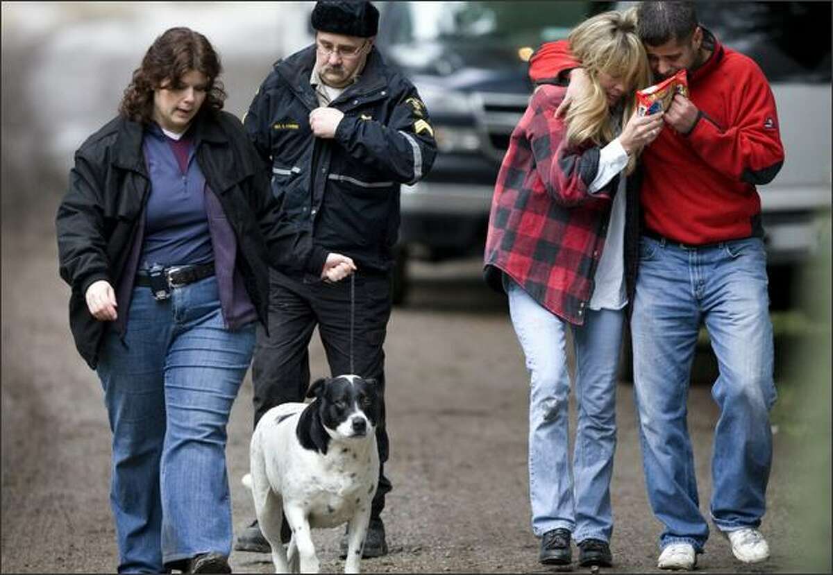 King County Sheriff's Detective Robin Cleary leads a dog, followed by King County Animal Control Sgt. Steve Couvion, near the house on the outskirts of Carnation where six people were shot to death on Christmas Eve. At right are Mary and Ben Anderson, relatives of those killed.