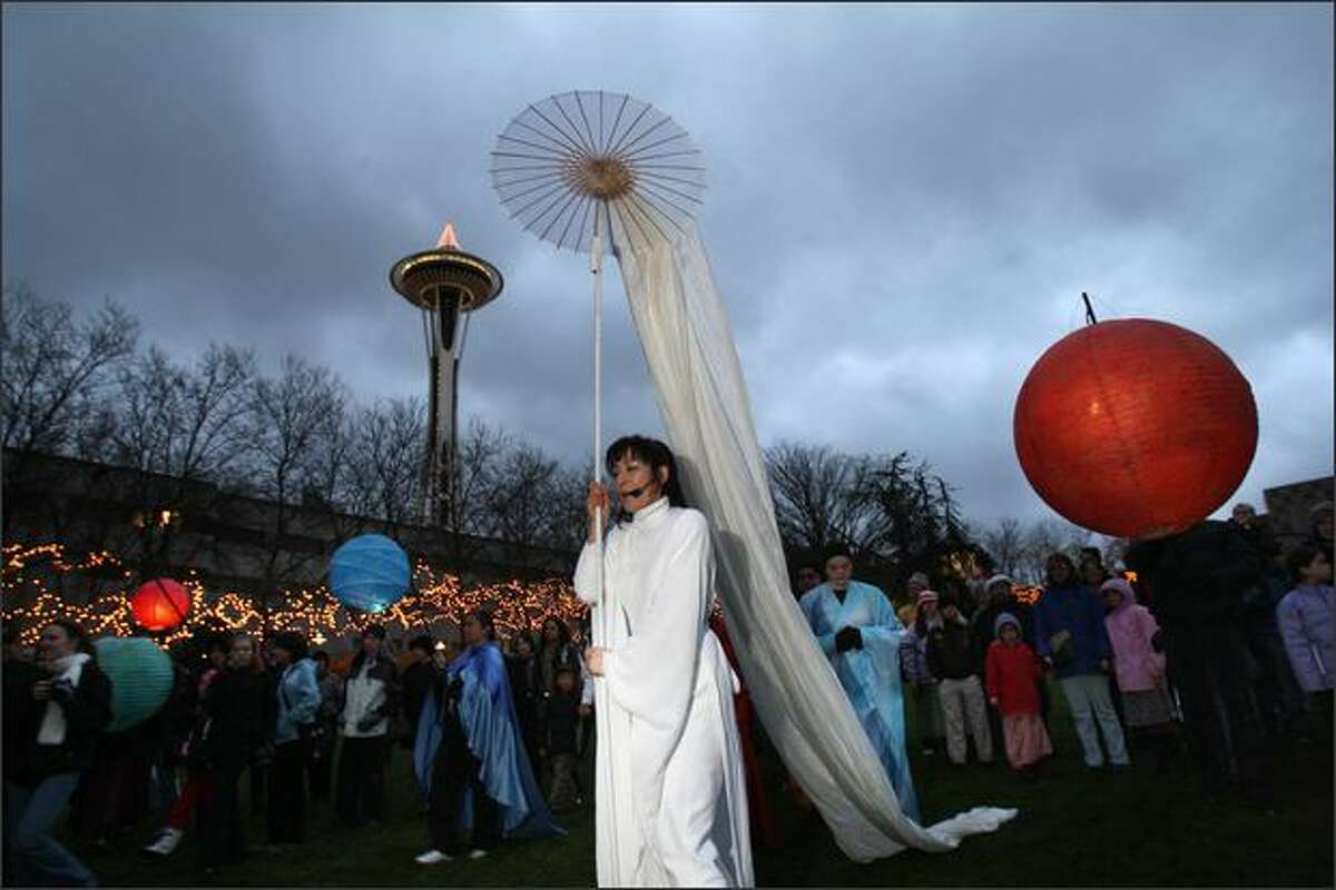 Representing winter, Naho Shioya leads brightly lit lanterns representing planets and a crowd of onlookers around the Seattle Center. The performance called "Orbis" directed by Manual R. Cawaling celebrated the winter Solstice, the shortest and darkest day of the year, and featured music, fire dancers, spoken words, and luminaria.