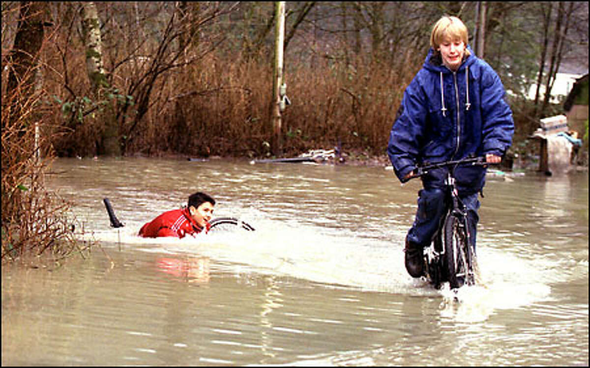 Brandon Irving, left, and Derik Shooster horse around in the water at a flooded trailer park on the Skagit River at Hamilton. They were on the way home from school when they decided to cruise a patch of water. Brandon hit a hole and got drenched. Rivers were on the rise in Western Washington yesterday, and some houses were flooded.