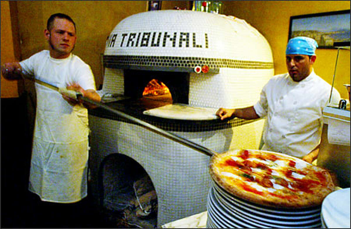 Pizzaiolo "Dino" (Espedito Santonicola, right) looks on as apprentice pizzaiolo Kevin Wittman, left, removes a pizza from the wood-burning dome at the Via Tribunali on Capitol Hill.