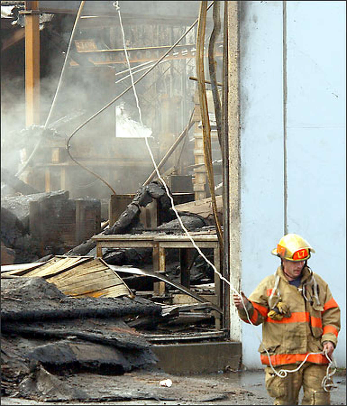 A Seattle firefighter drags a line that guides an overhead nozzle in an effort to put out a still-smoldering fire at Capital Industries, a Georgetown metal-fabricating company. The main building of the third-generation family business was destroyed by the blaze Sunday.